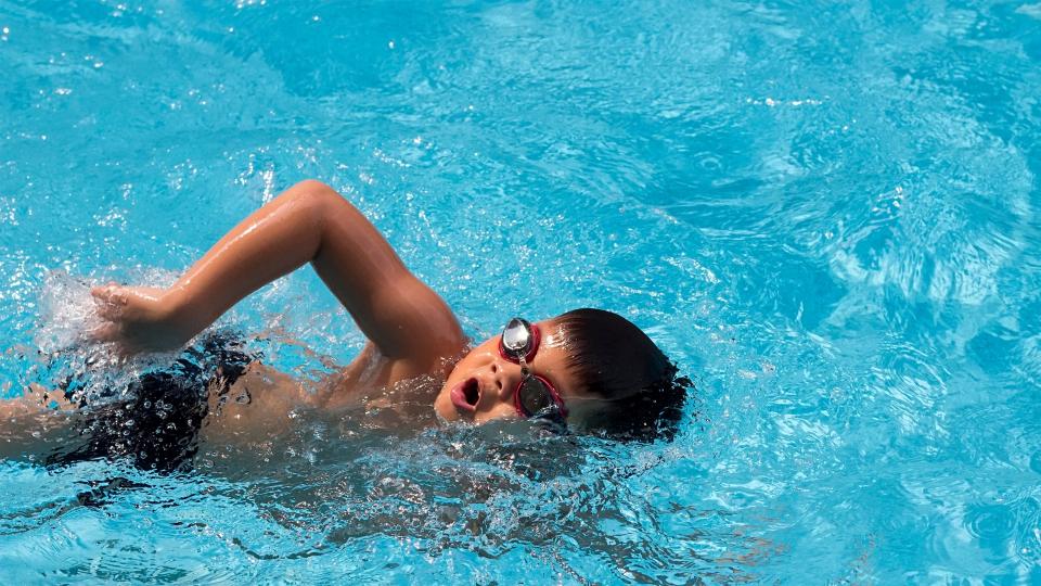 A young boy happily swimming in a pool, enjoying the cool water on a sunny day.