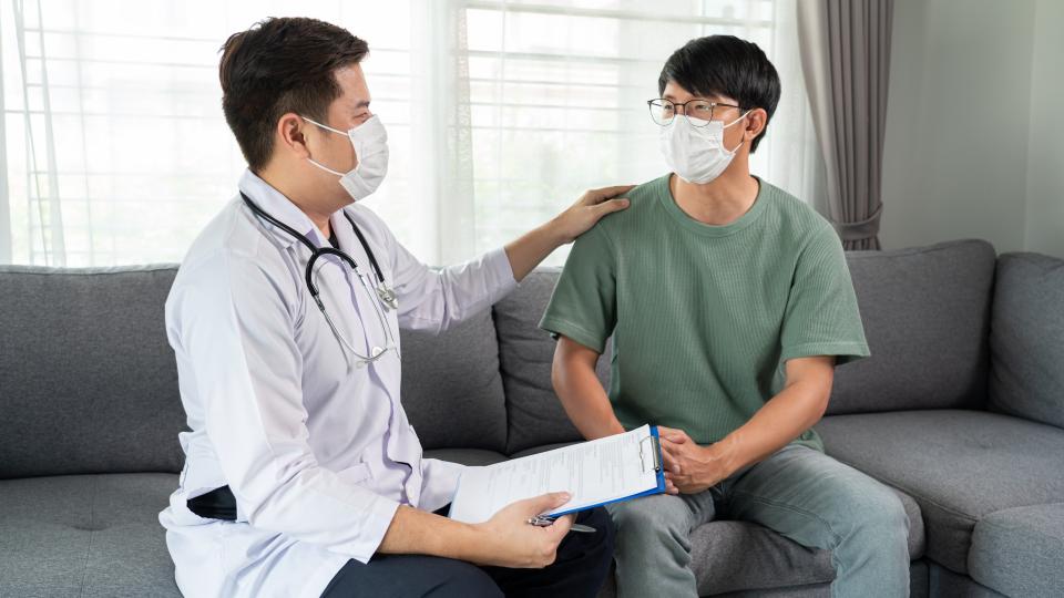 A man wearing a mask and holding a clipboard, accompanied by a doctor.