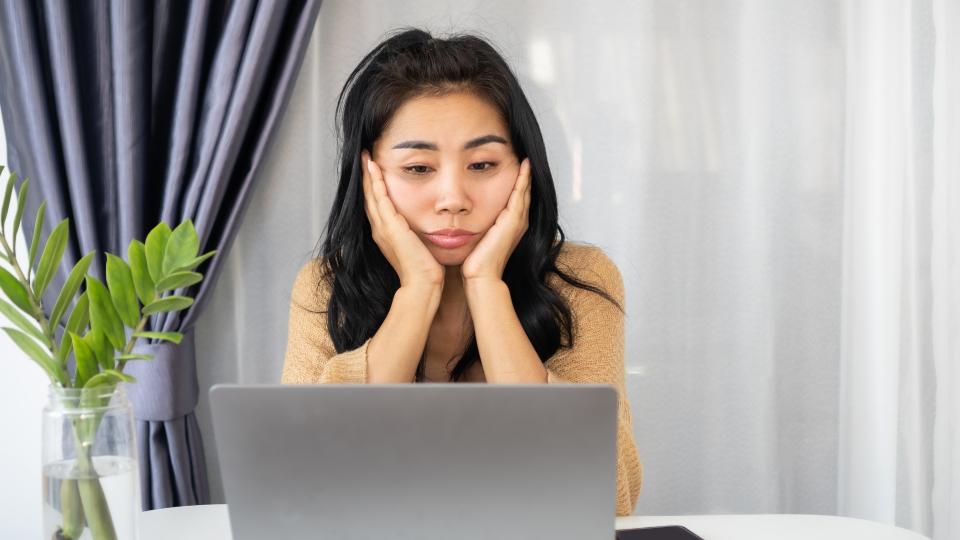 A woman sitting at a table with her hands covering her face in frustration.