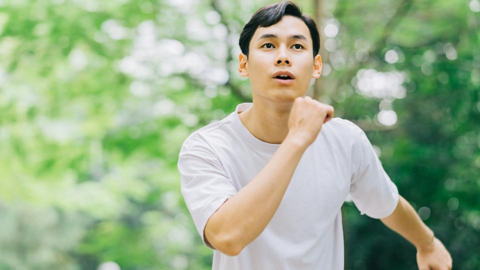 A man jogging in a park, surrounded by lush greenery and trees, enjoying a healthy outdoor activity.