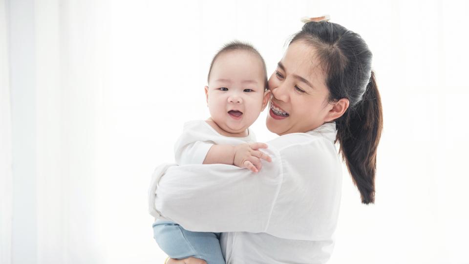 A smiling woman holding a baby in her arms.