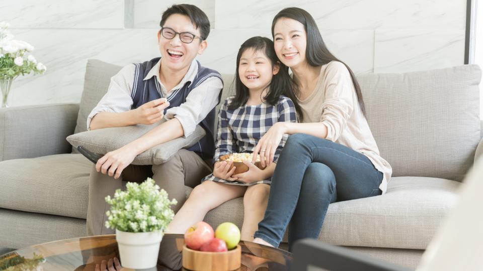 A family sitting on a couch, engrossed in watching TV together.