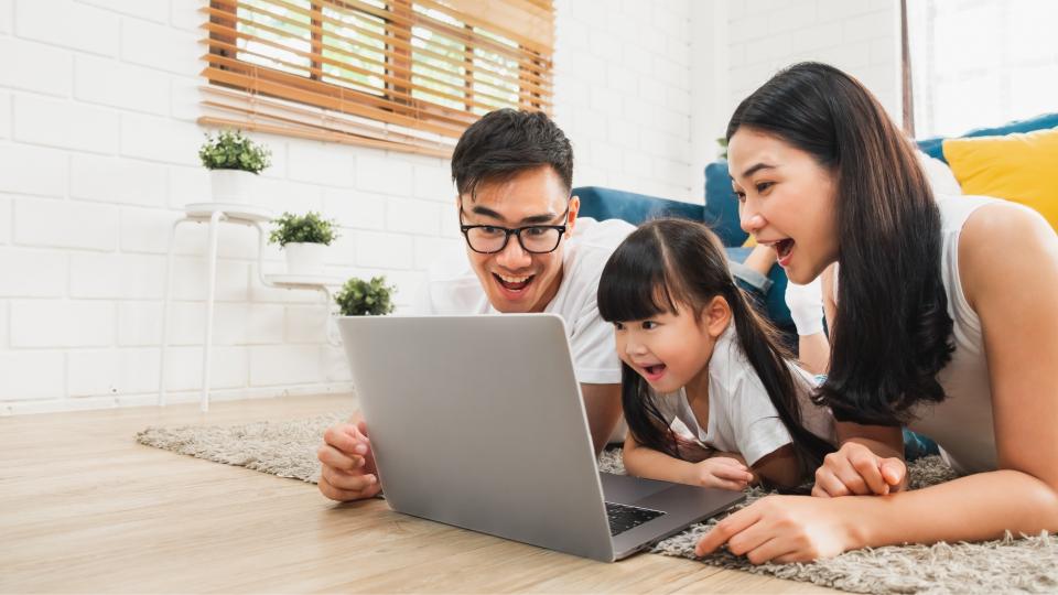 A family sitting on the floor, gathered around a laptop, engaging in a digital activity together.