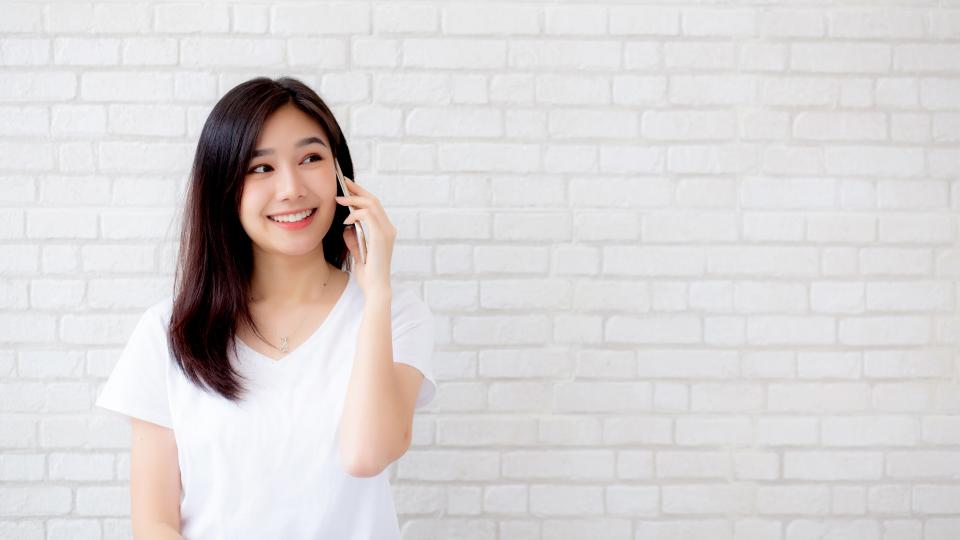 A woman chatting on cellphone in front of white brick wall.