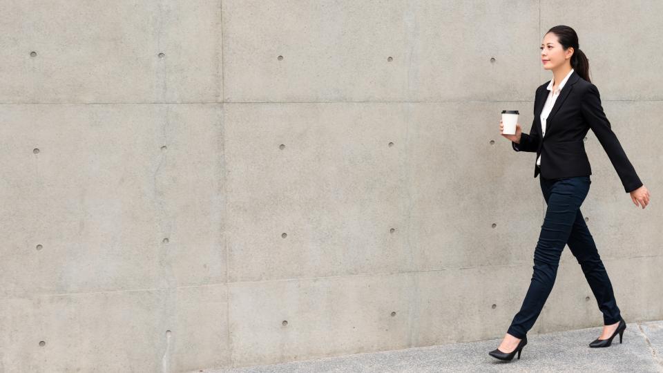 A professional woman in a business suit walking briskly while holding a coffee cup. Self-Esteem