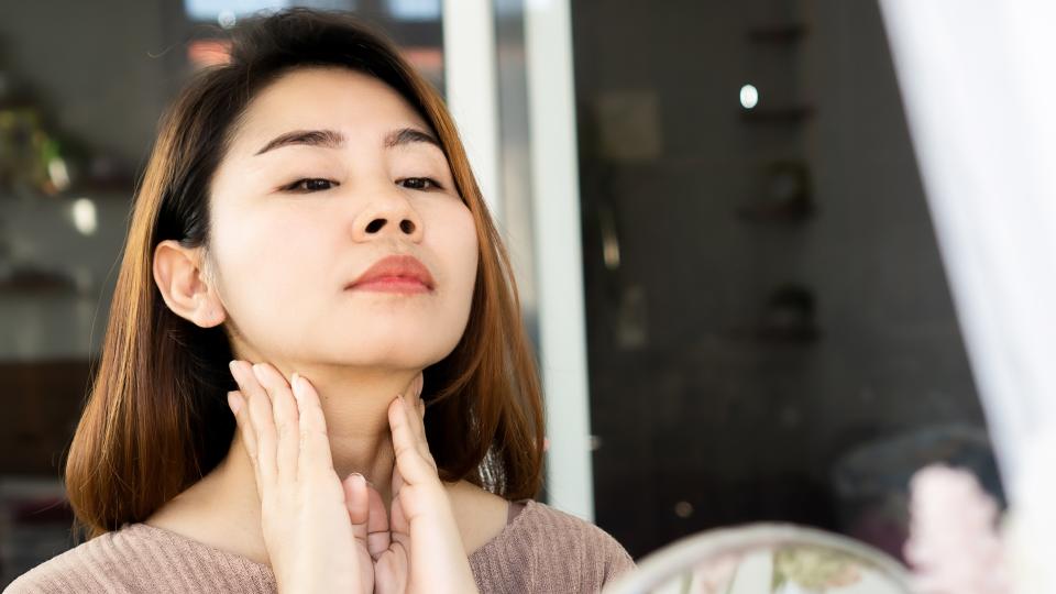 A woman examining her neck in the mirror, possibly checking for any imperfections or signs of aging.