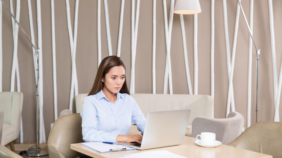 A woman sitting at a table with a laptop, typing on the keyboard.