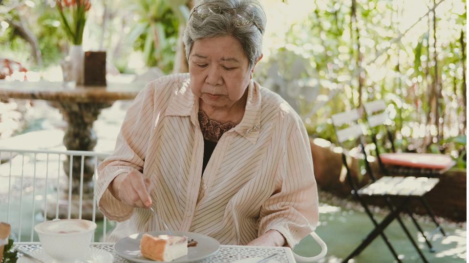 Elderly woman enjoying cake and coffee at a table.