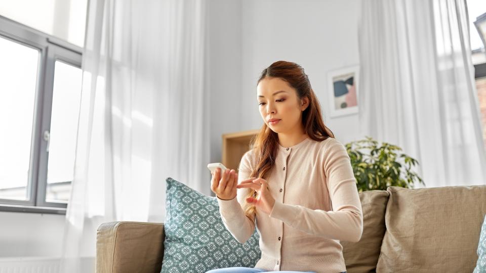 A woman engrossed in her phone while sitting on a couch. Manage Diabetes