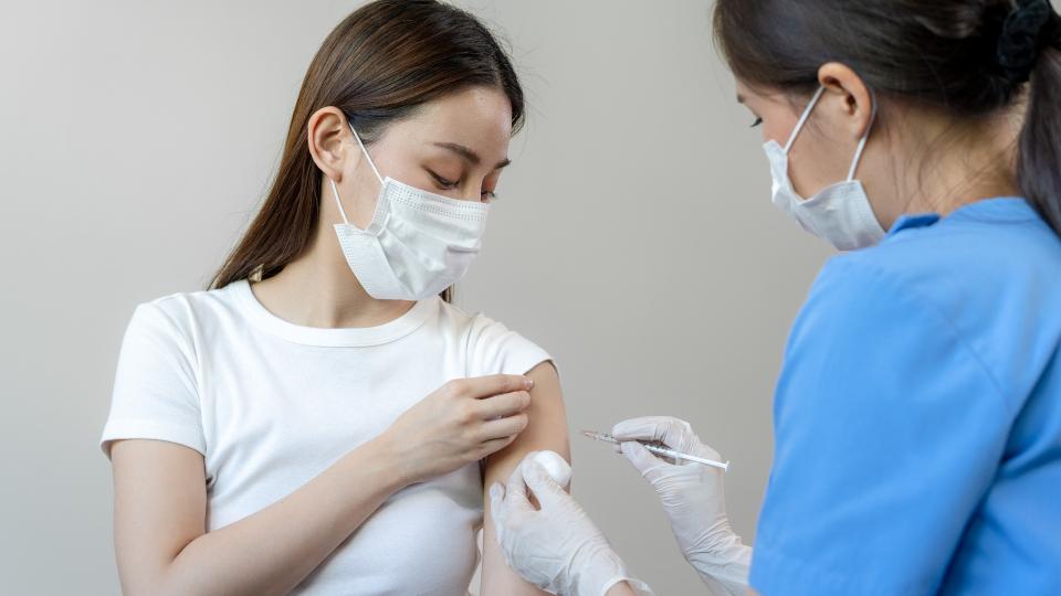 A woman receiving a vaccine shot from a nurse in a medical setting.