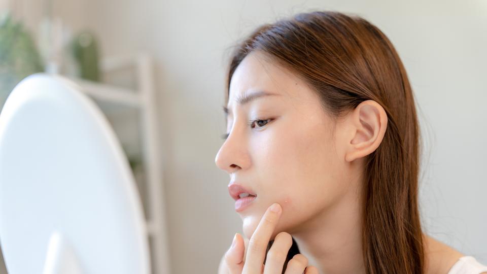 A woman examining her reflection in a mirror, focusing on her facial features. Self-Esteem