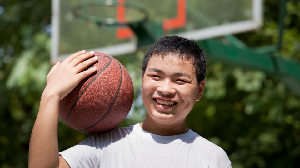 A young boy confidently holds a basketball, ready to shoot or dribble. His focus and determination are evident in his stance.