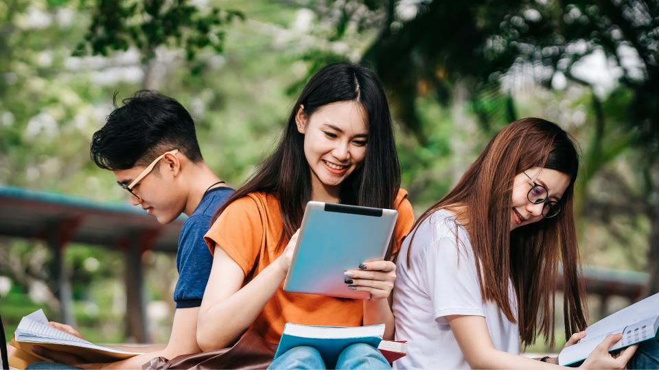 Three young students sitting on a bench, focused on using a tablet.