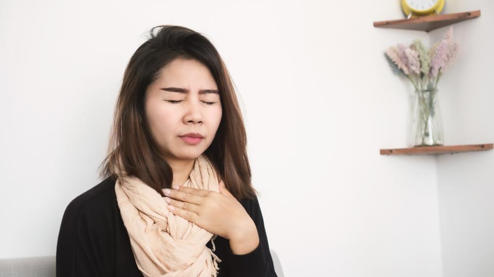 A woman clutching her chest in pain while sitting on a couch in a living room.