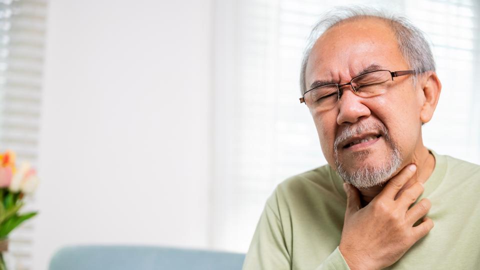 A man holding his throat in discomfort, showing signs of a sore throat. Chronic Tonsillitis