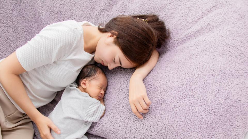 Woman laying on top of a baby, both peacefully sleeping.