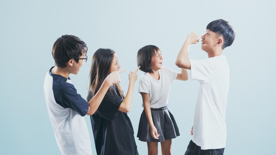 Four young people standing together, one pointing to his nose.