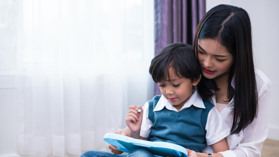 Woman and child sitting on floor, engrossed in tablet.