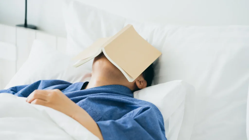 A person enjoying a cozy moment in bed, hiding behind a book for some peaceful reading time.