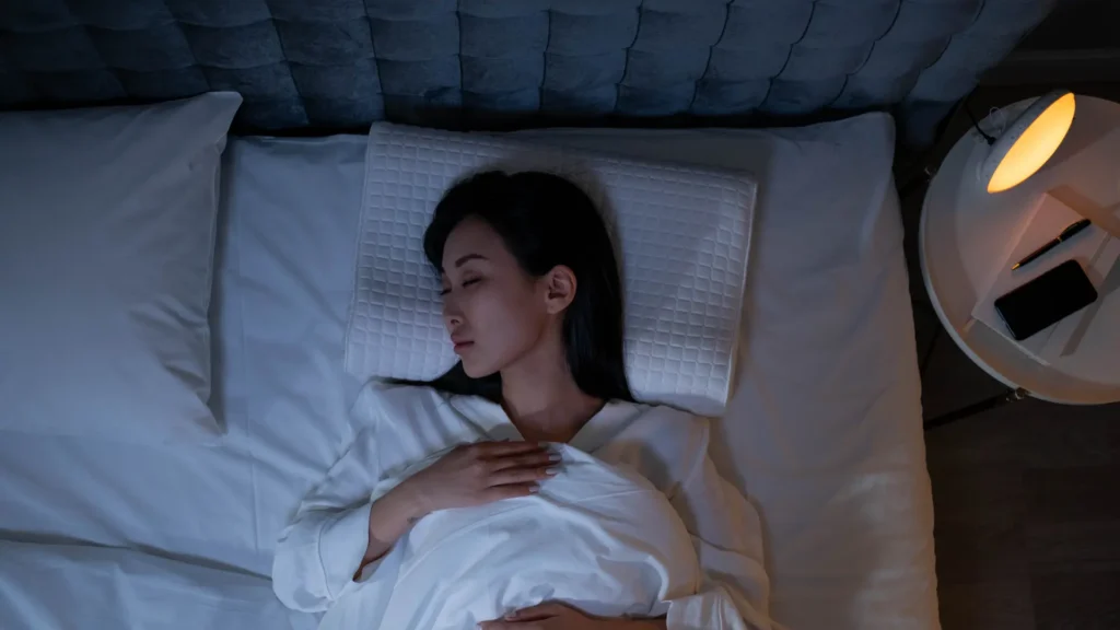 A woman peacefully sleeping in bed with calming light illuminating the room.