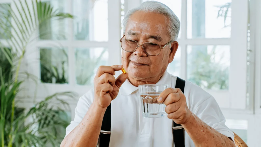 An elderly man holds a glass of water, quenching his thirst.