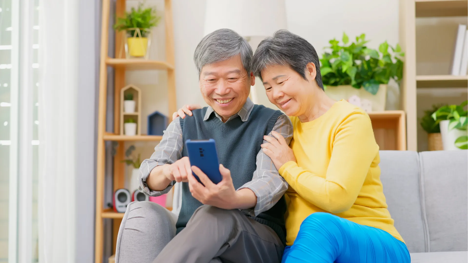 An elderly couple on a couch, engrossed in a cell phone.
