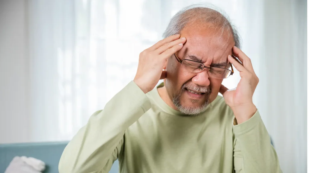 Warning Signs of Dementia? A man with glasses and a green shirt looks distressed as he holds his head.