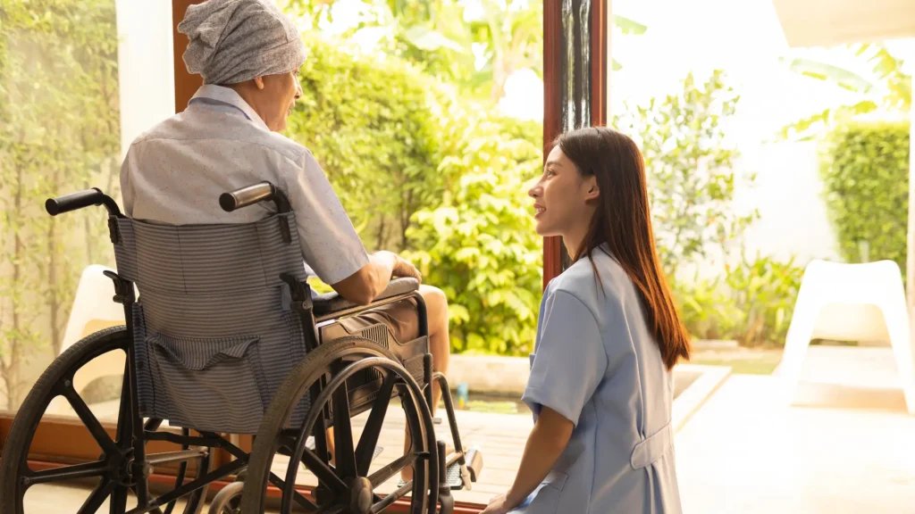 A elderly man in a wheelchair conversing with a nurse, displaying empathy and support in a healthcare setting.