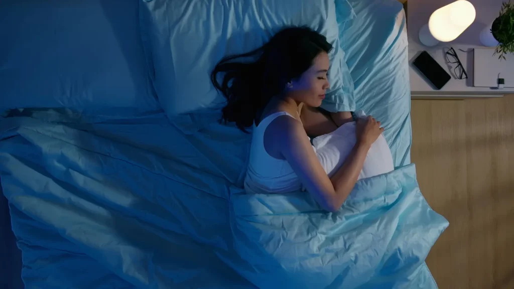 A woman peacefully resting in bed with blue sheets.