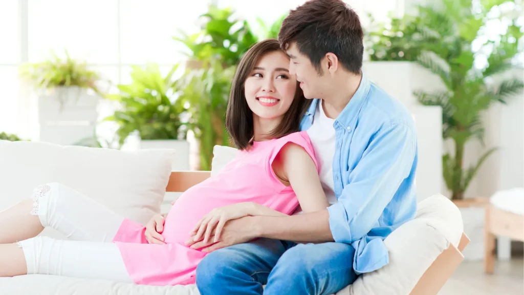 A pregnant woman and her husband sitting on a couch, eagerly awaiting the arrival of their baby.