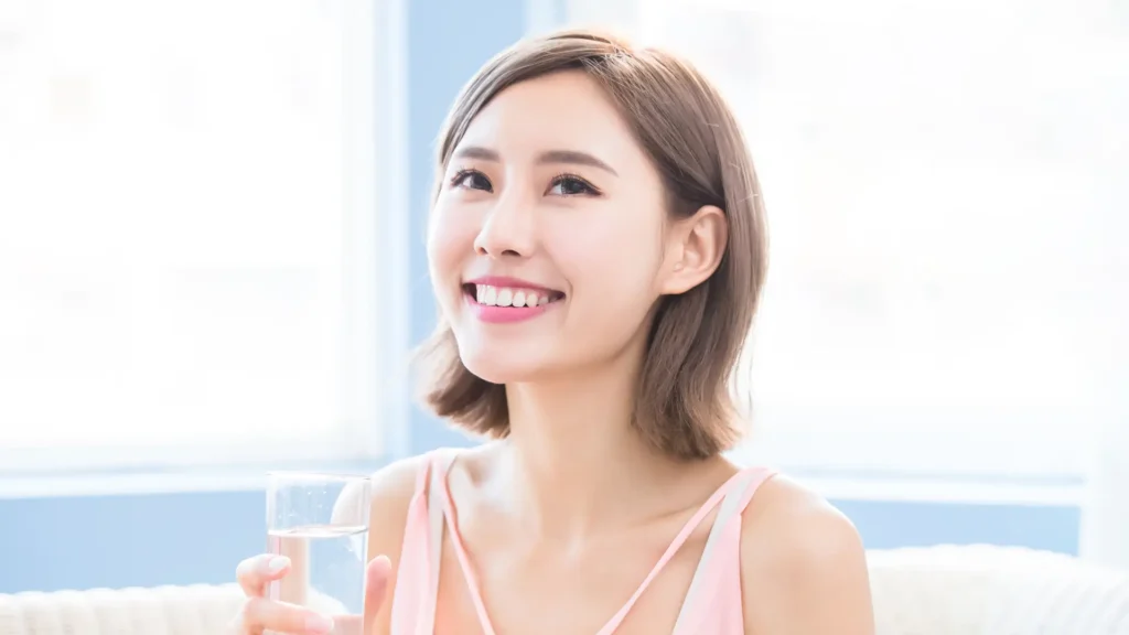 A woman happily holds a glass of water, radiating joy with her smile.