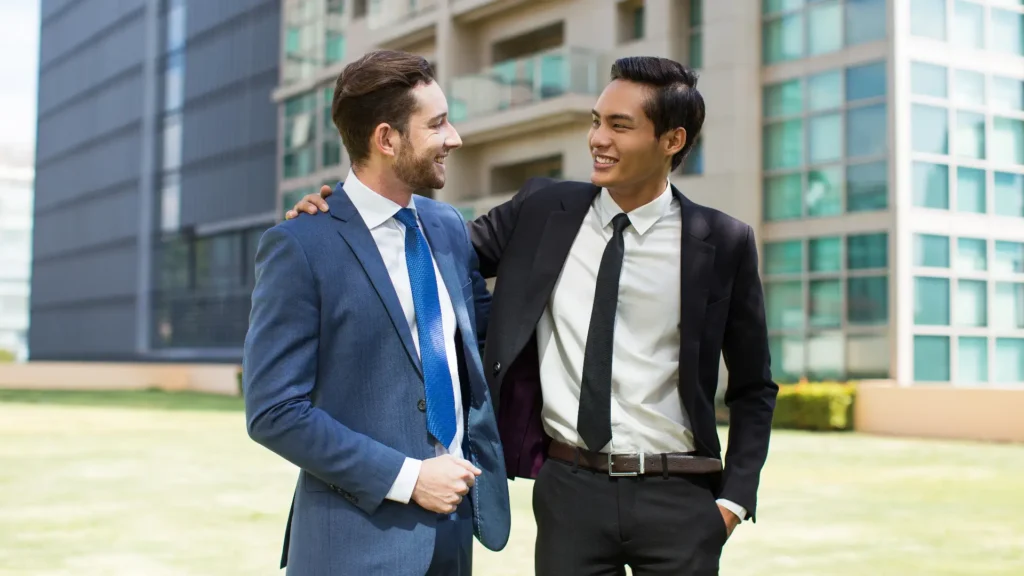 Two businessmen in suits standing outside a modern office building. Supportive Network