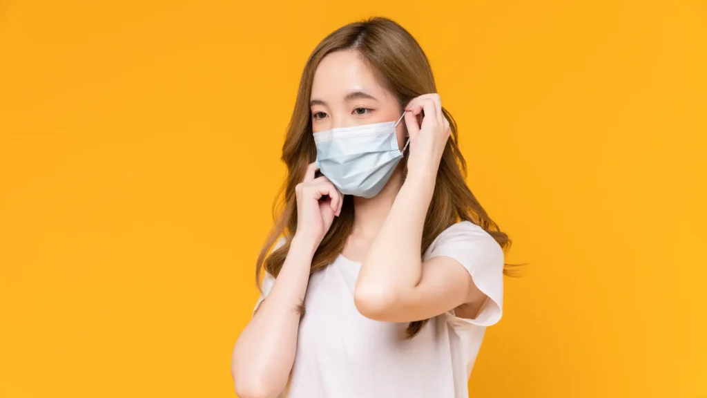 Woman wearing a surgical mask on orange background, protecting herself from germs and viruses.