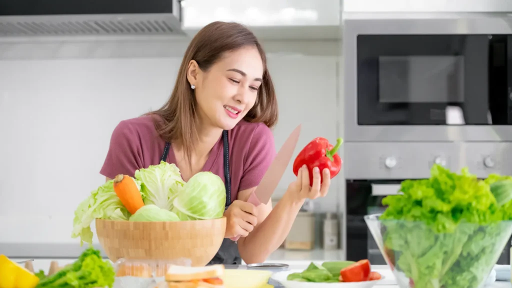 Woman holding red pepper and bowl of vegetables, preparing healthy meal.