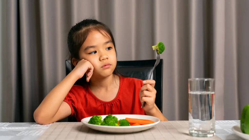 Little girl sitting at a table with a plate of vegetables.