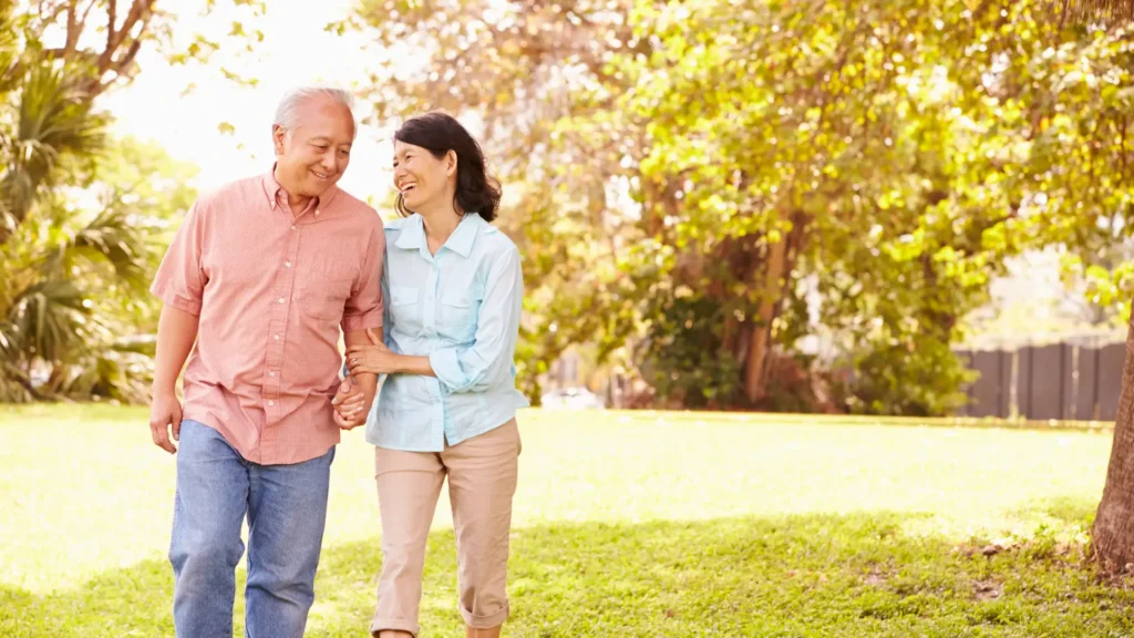 An elderly couple strolling through a serene park, enjoying each other's company amidst nature's beauty.