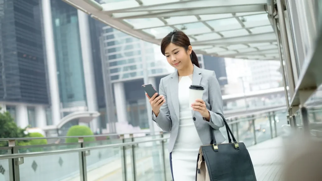 A businesswoman multitasking in the city, using her mobile phone while holding a coffee cup.