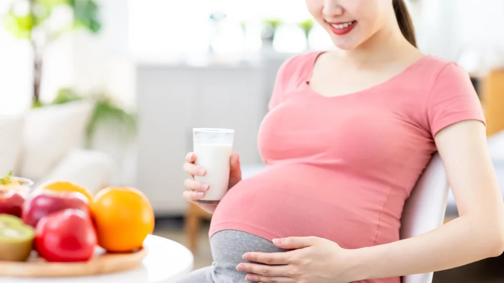 A pregnant woman enjoying a glass of milk and eating fresh fruit.