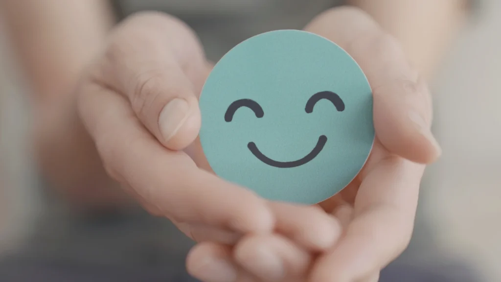 Person holding a smiley face sticker, symbolizing happiness and positivity.