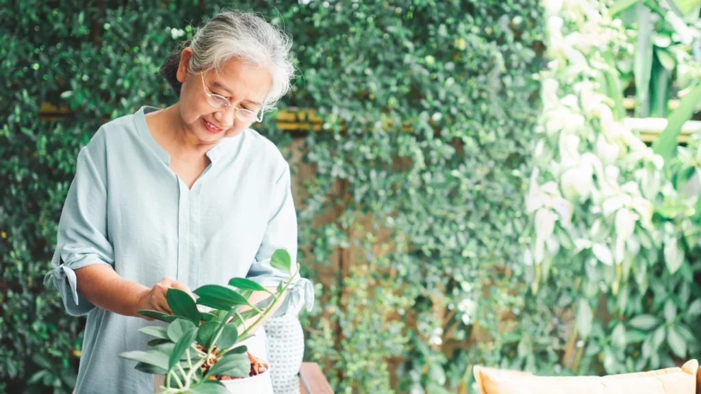 Elderly woman gently cradles a potted plant in her hands.