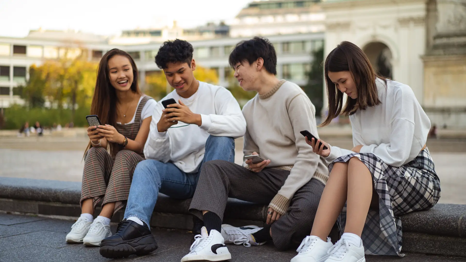 Four friends sitting on a bench, engrossed in their phones. Enjoying each other's company while staying connected in the digital world.