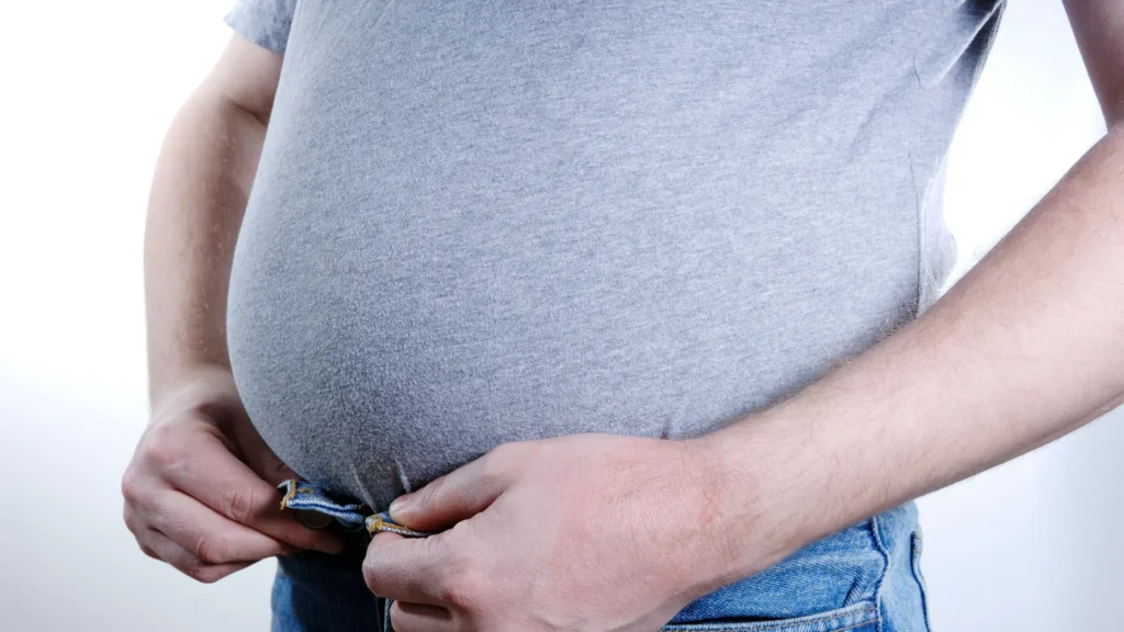 A man in jeans clutching his stomach in discomfort.