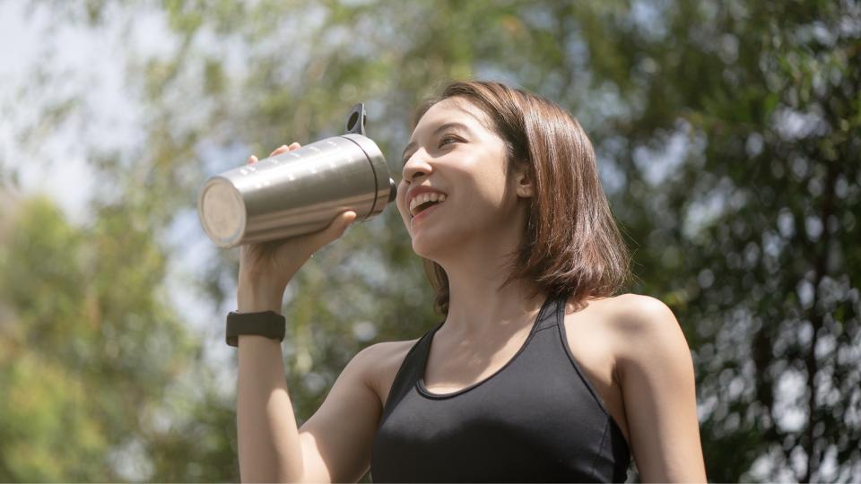 Woman drinking from metal cup outdoors.