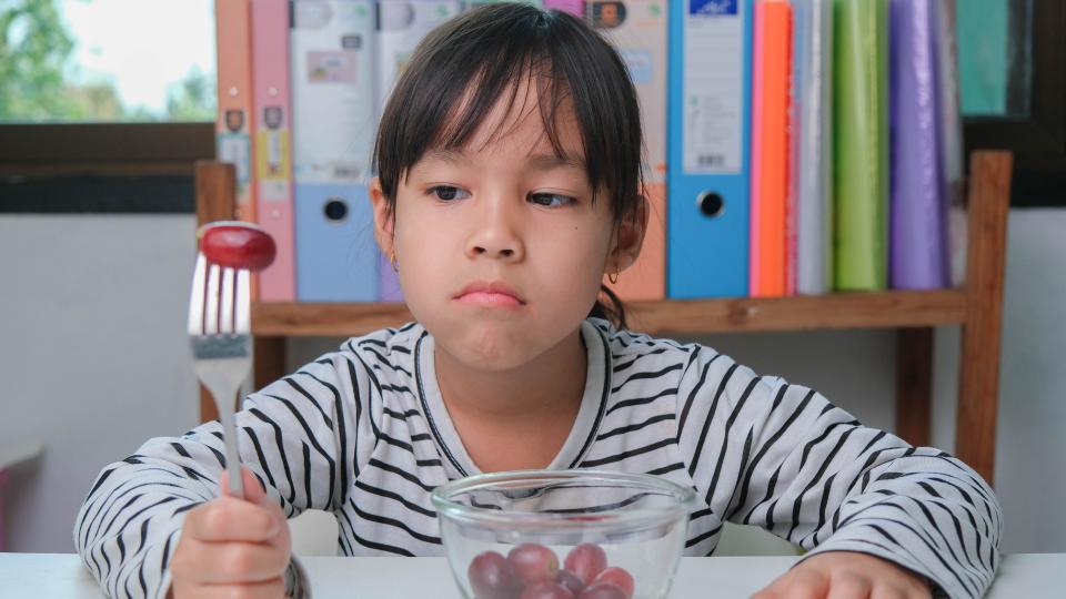 A little girl eagerly holds a fork and knife, ready to dig into a bowl of delicious cherries.