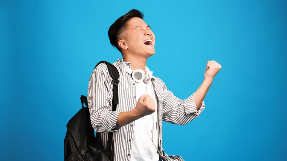 A man wearing headphones and a backpack, joyfully celebrating with arms raised in the air.