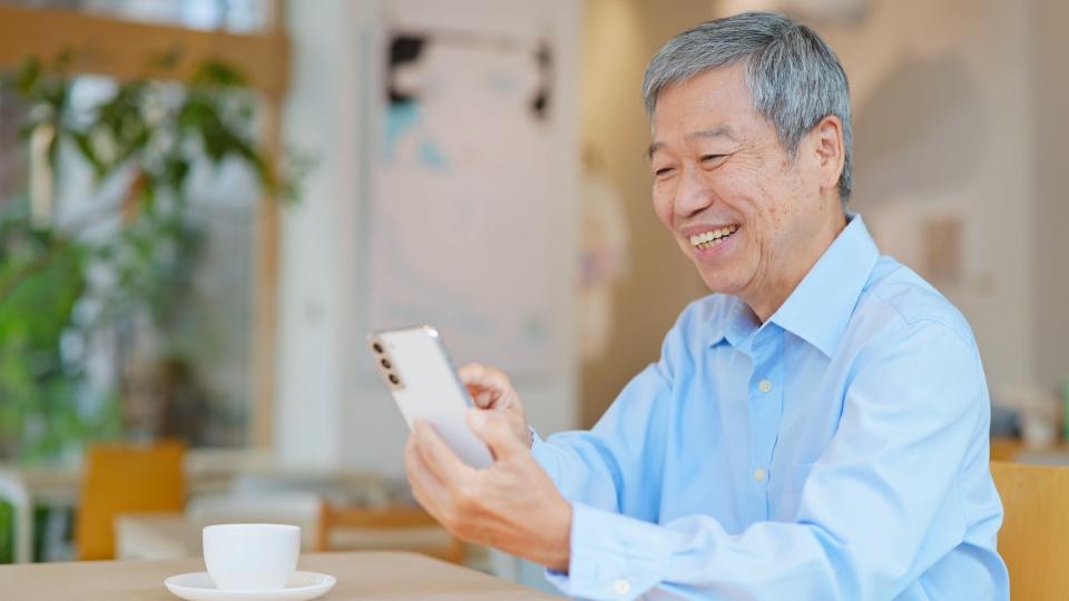 An elderly man happily using his phone, displaying a warm smile.