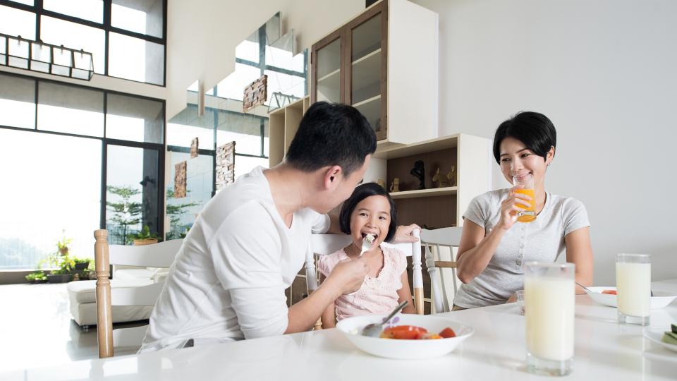 A man and a woman enjoying breakfast with a child at the dining table.