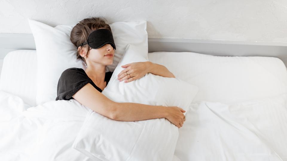 A woman peacefully sleeping in bed with a blindfold on. Improve Sleep Quality