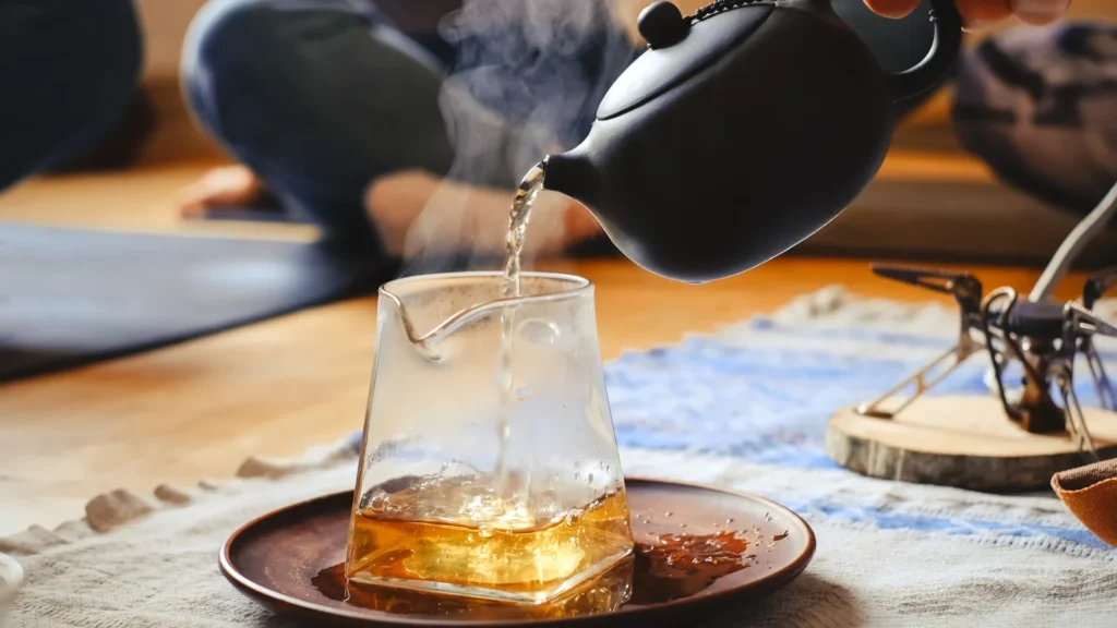 Pouring tea from a teapot into a glass on a table.