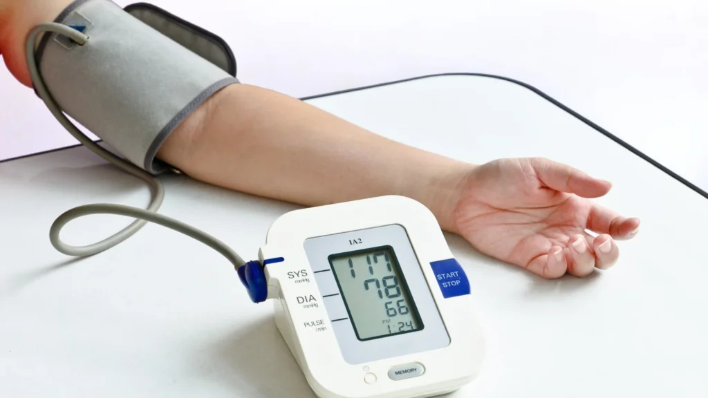 A person holding a blood pressure monitor on a table. High Blood Pressure